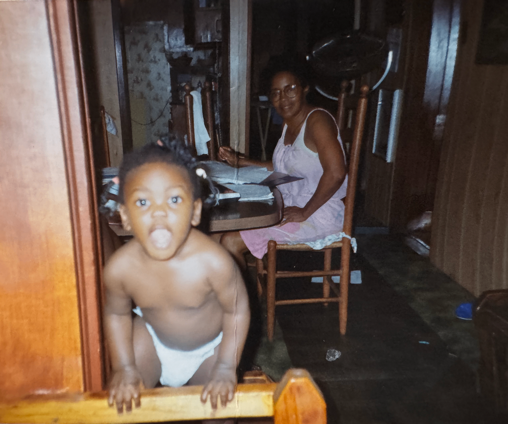 A grandmother sorting papers at the dining table while a toddler stands nearby